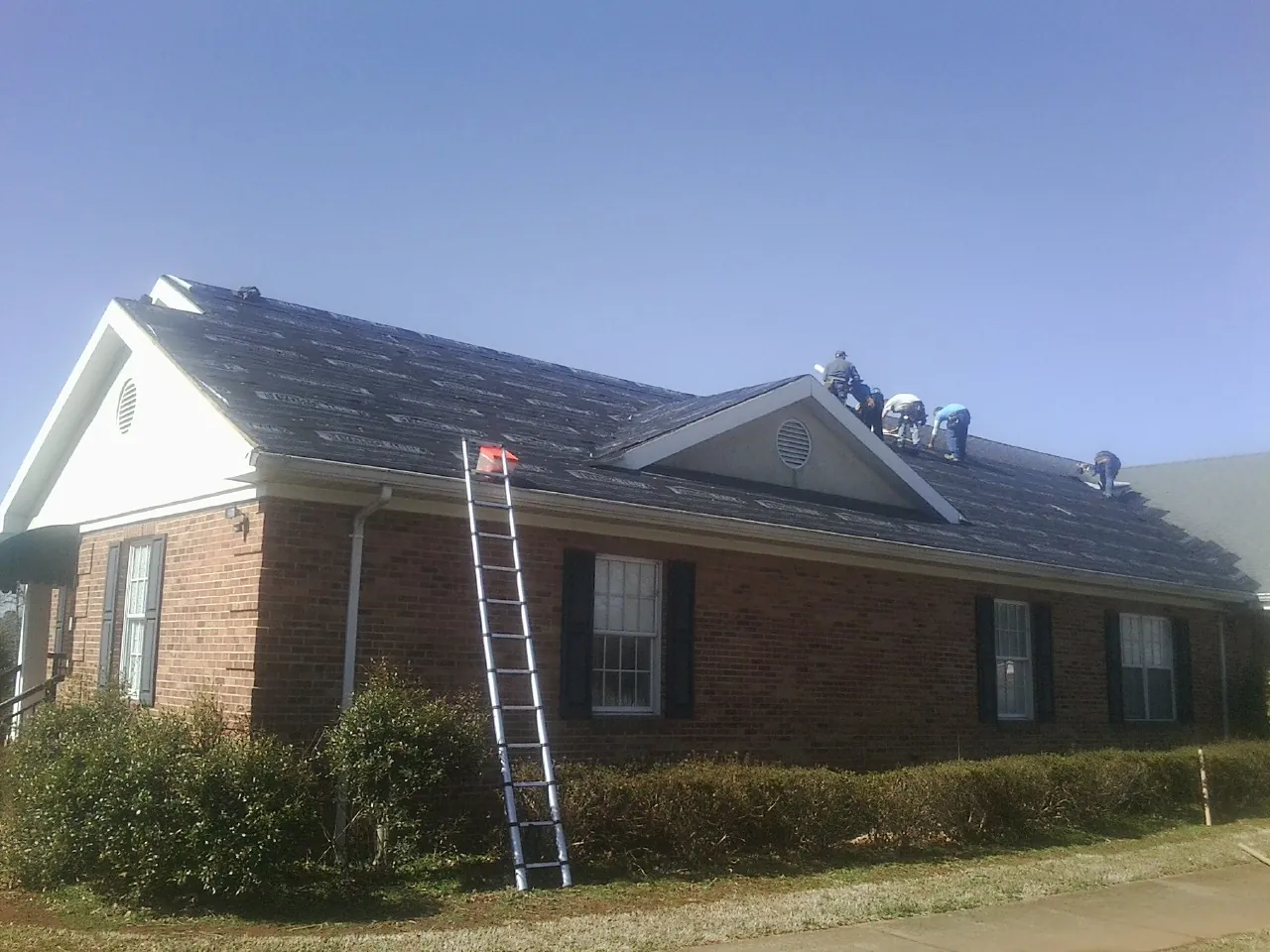 Crew tearing shingles off a brick ranch roof with a ladder set — Emergency Roof Repair work by our crew in Lindon