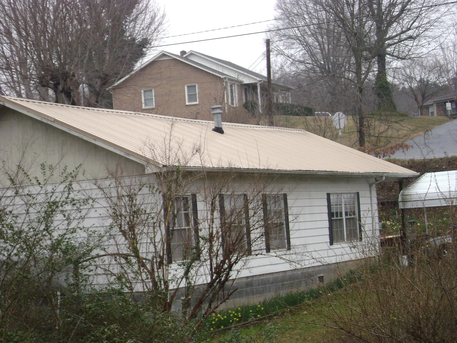 Tan metal roof on a white sided house set into a hillside — Commercial Roofing by Roofing Brothers in Lindon