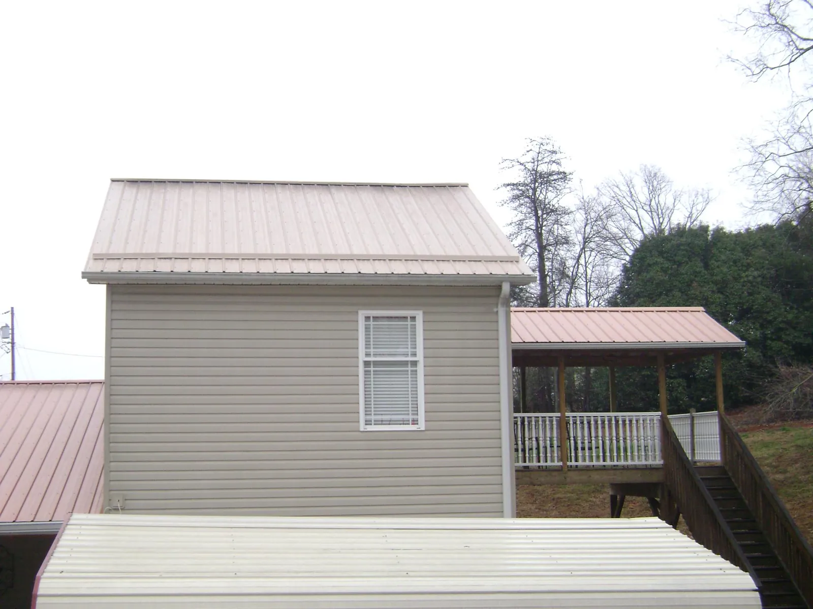 Tan metal roofs on a two story addition and attached porch, from a Roof Replacement job in Lindon